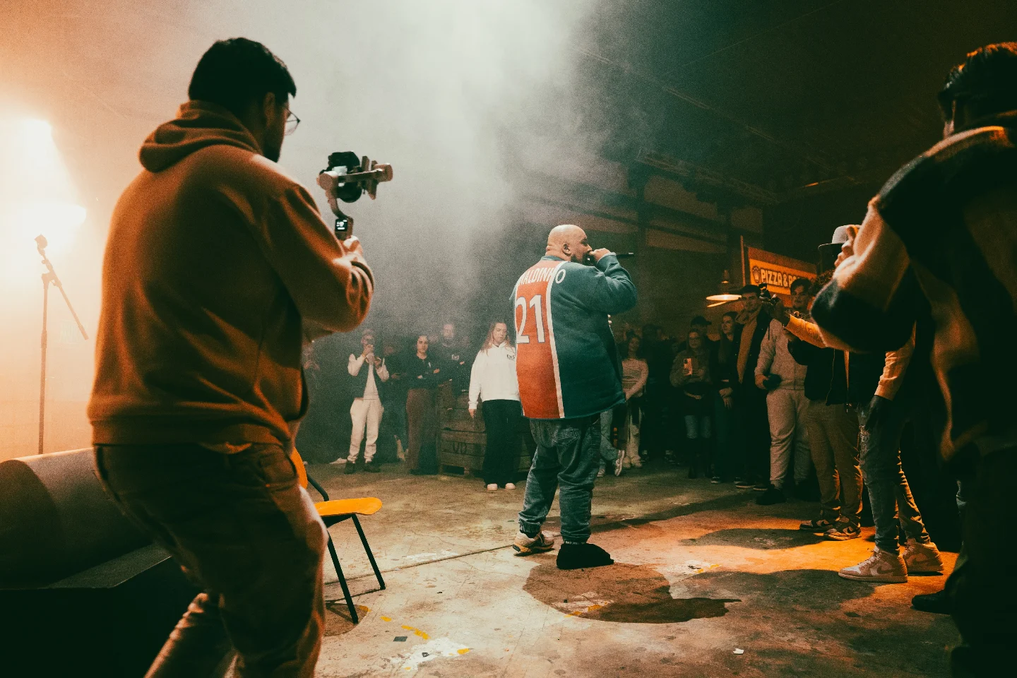 A rapper performs for the crowd in a hall at High Rollers while a cameraman films